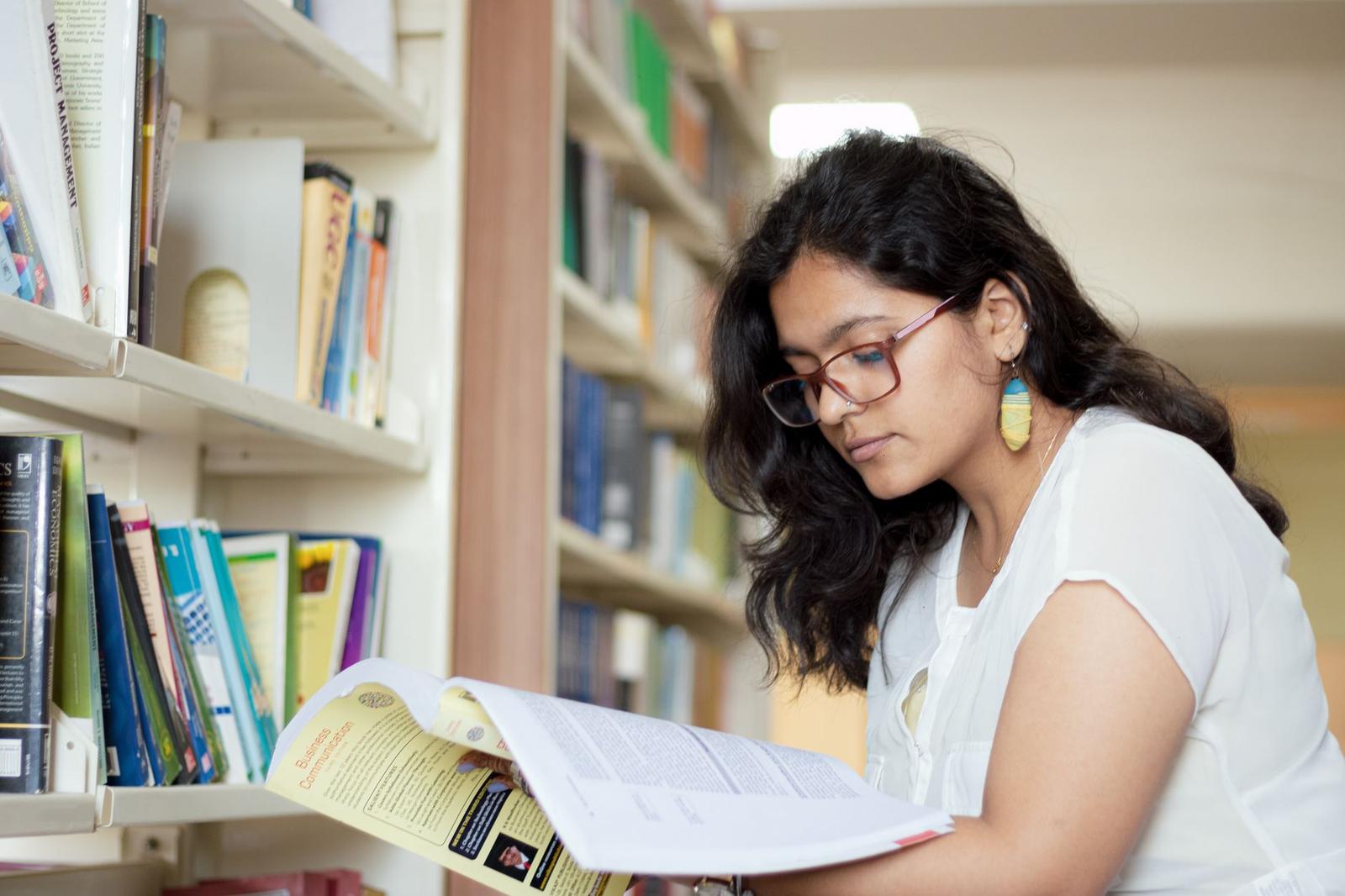 Portrait of a Smiling Young Indian Student Reading a Book in a Library
